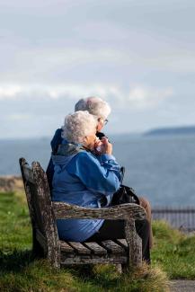 Two elderly people sitting on a bench looking at the sea